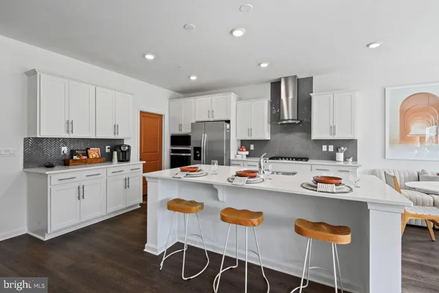 a kitchen with stainless steel appliances granite countertop a stove a sink a refrigerator and white cabinets with wooden floor