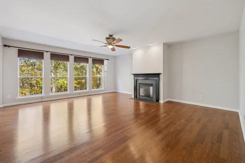 an empty room with wooden floor chandelier fan and windows