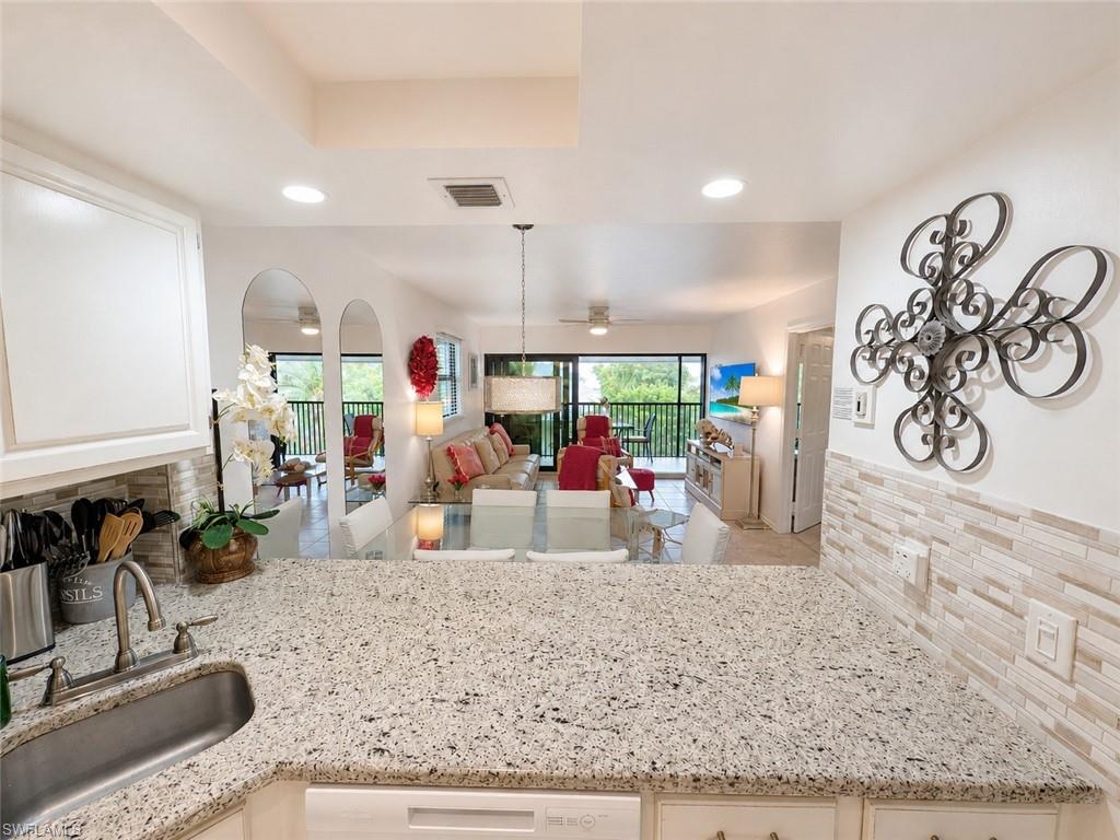 600 Neapolitan Way, Unit 449 Naples, FL 34103 - Photo 10 of 44 Kitchen featuring granite countertops, a stainless steel sink with a gooseneck faucet, white cabinetry, and a subway tile backsplash