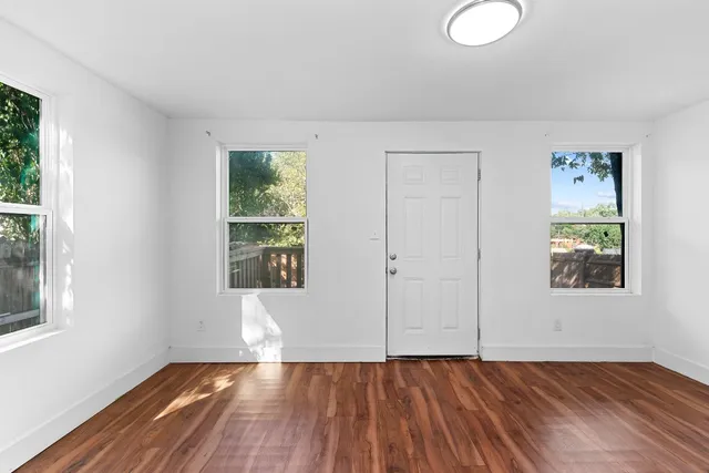 a view of an empty room with wooden floor and a window