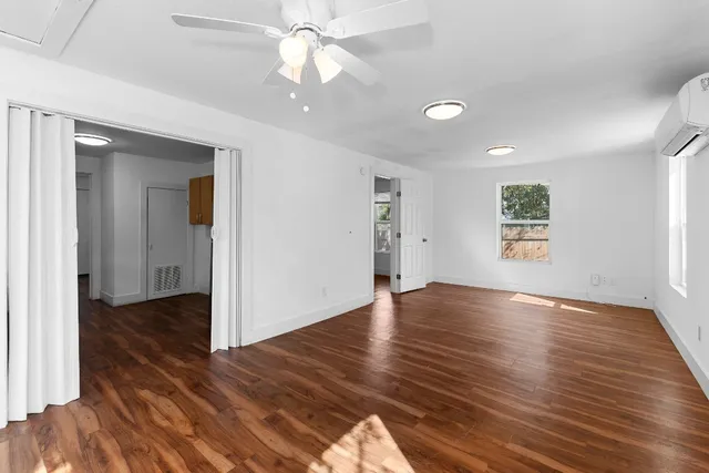 an empty room with wooden floor chandelier fan and windows