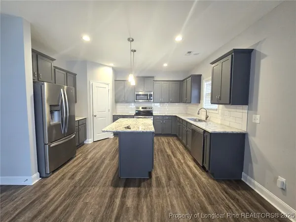 a kitchen with kitchen island granite countertop a sink refrigerator and wooden cabinets