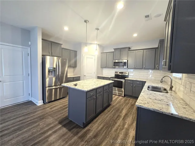 a kitchen with stainless steel appliances granite countertop wooden cabinets a refrigerator a sink a stove a microwave and wooden floors