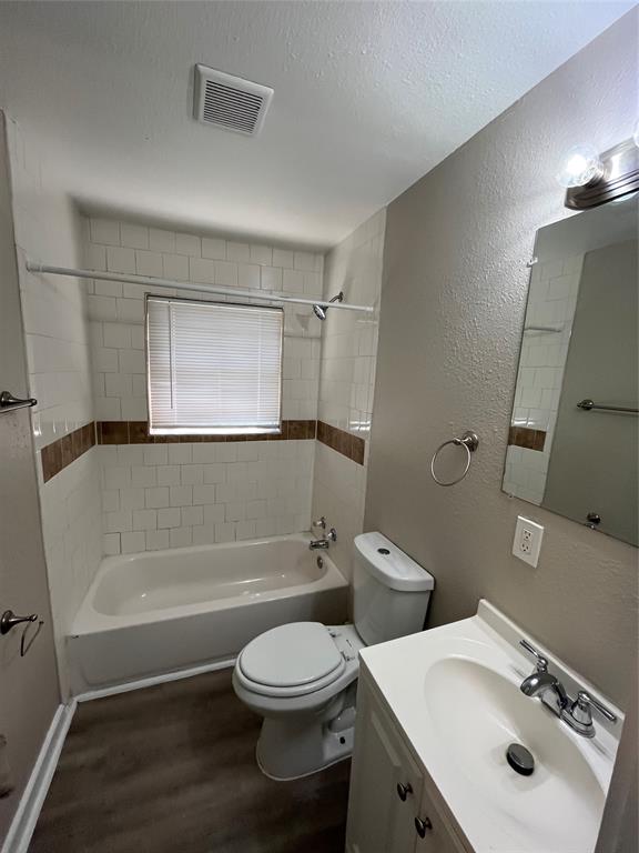 1316 North Prairie Creek Road Dallas, TX 75217 - Photo 9 of 19 Full bathroom featuring a white bathtub, ceramic tile surround with decorative accent, a toilet, and a vanity with an integrated sink