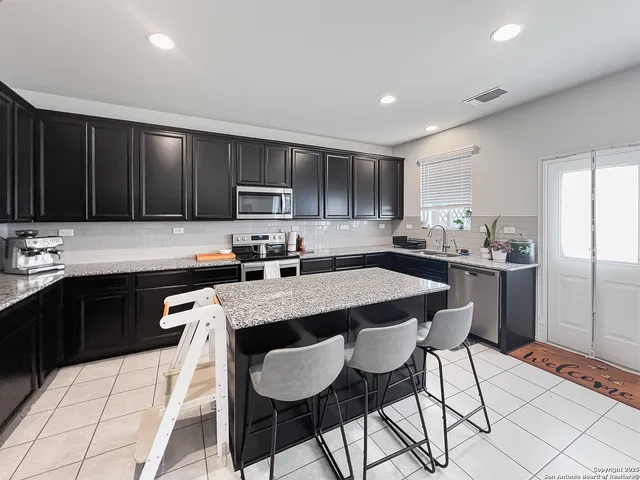 a kitchen with stainless steel appliances granite countertop a sink a stove a refrigerator cabinets and chairs