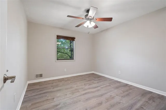 an empty room with wooden floor chandelier fan and windows