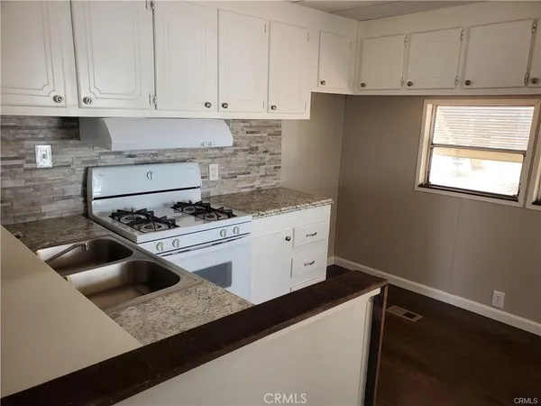 a kitchen with granite countertop a sink dishwasher a stove and white cabinets