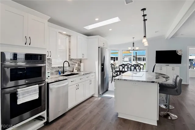 a kitchen with stainless steel appliances kitchen island granite countertop a stove top oven a sink dishwasher and a refrigerator with wooden floor