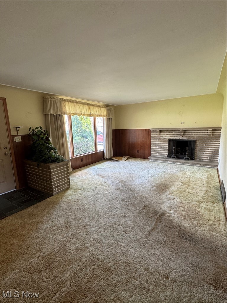 3919 New Road Youngstown, OH 44515 - Photo 2 of 16 Unfurnished living room featuring wooden walls, carpet floors, a wainscoted wall, and a brick fireplace