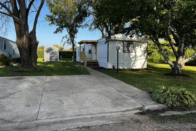 a view of a white house next to a yard with a large tree