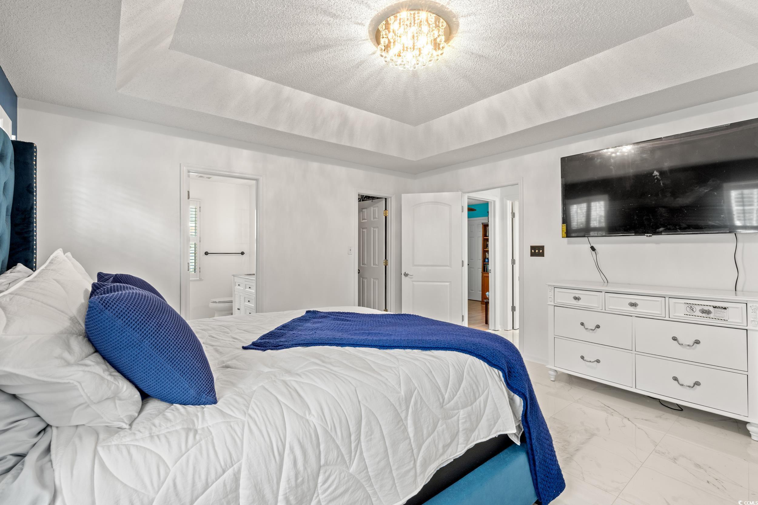 3056 Sweetpine Lane Conway, SC 29527 - Photo 25 of 36 Bedroom featuring a tray ceiling, a textured ceiling, light marble finish flooring, connected bathroom, and a chandelier