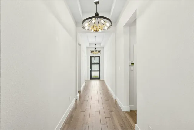 a view of a hallway with wooden floor and a chandelier