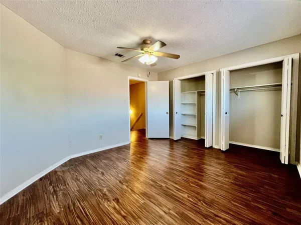 an empty room with wooden floor closet fan and windows