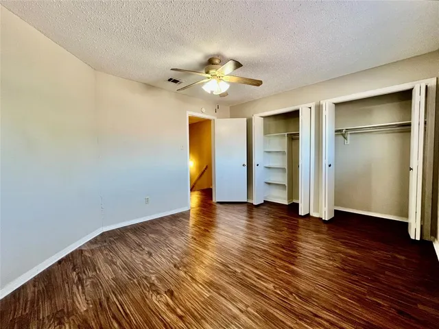 an empty room with wooden floor closet fan and windows