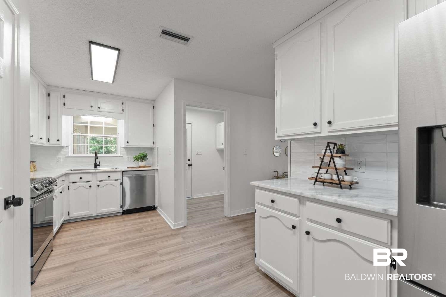 10251 Windmill Road Fairhope, AL 36532 - Photo 27 of 44 Kitchen featuring appliances with stainless steel finishes, backsplash, white cabinetry, and light wood finished floors