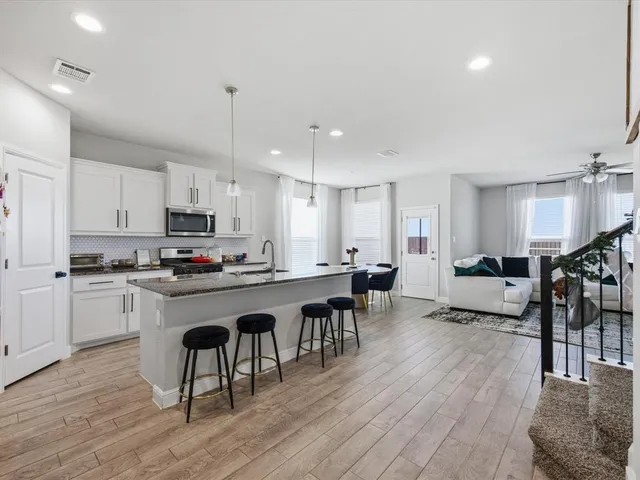 a open kitchen with stainless steel appliances granite countertop a dining table chairs stove a refrigerator and cabinets