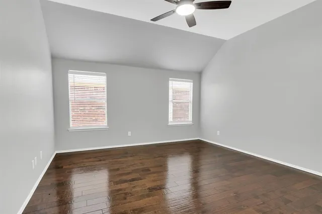 an empty room with wooden floor chandelier fan and windows