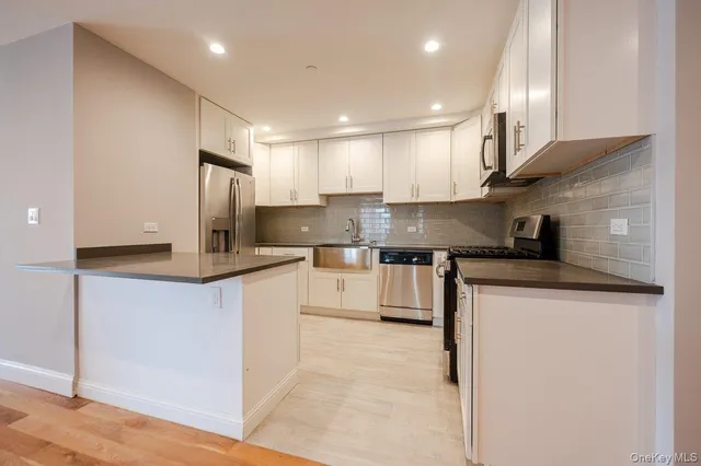 a kitchen with stainless steel appliances granite countertop a sink a stove a refrigerator and white cabinets