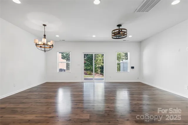 an empty room with wooden floor chandelier fan and windows