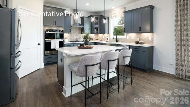 a kitchen with stainless steel appliances kitchen island granite countertop a refrigerator a stove a sink and a dining table with wooden floor