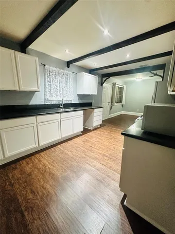 a kitchen with stainless steel appliances kitchen island granite countertop a sink dishwasher stove and white cabinets with wooden floor