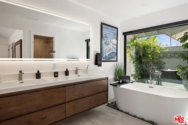 a bathroom with a double vanity sink a mirror and a bathtub next to a window
