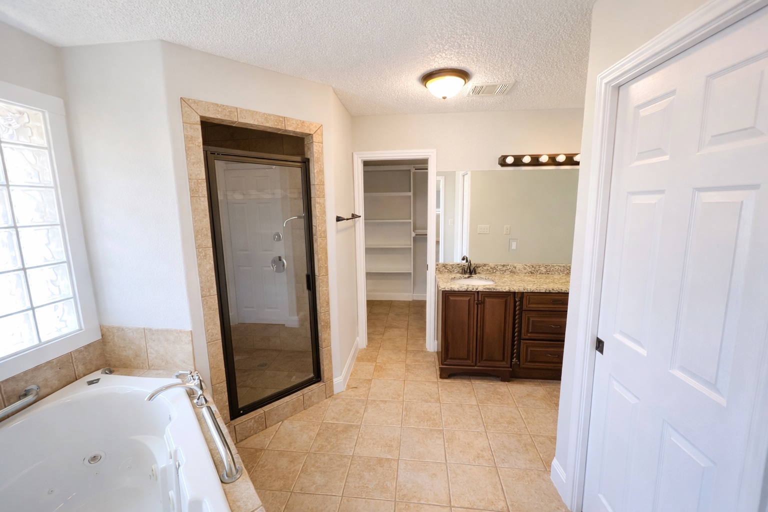 4500 Woodmoor Circle Austin, TX 78721 - Photo 2 of 6 Full bathroom featuring vanity, a whirlpool tub, a spacious closet, a textured ceiling, and a stall shower