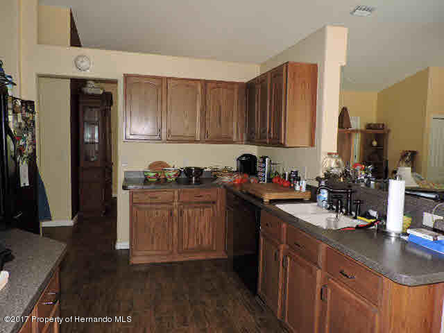 1156 Arlanie Road Brooksville, FL 34604 - Photo 11 of 27 a kitchen with stainless steel appliances granite countertop a refrigerator a sink dishwasher and wooden cabinets with wooden floor
