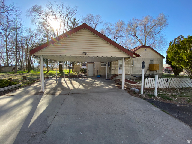 1766 Pine Rd Pine Canyon Tooele, UT 84074 - Photo 5 of 16 Carport with a red gabled roof and beige soffits, featuring a concrete driveway and an exterior door
