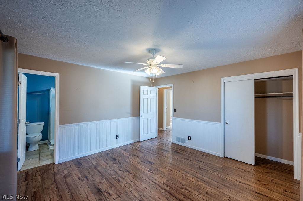 3601 River Road Vienna, WV 26105 - Photo 16 of 40 Unfurnished bedroom with dark wood-style floors, a textured ceiling, wainscoting, a ceiling fan, and a closet