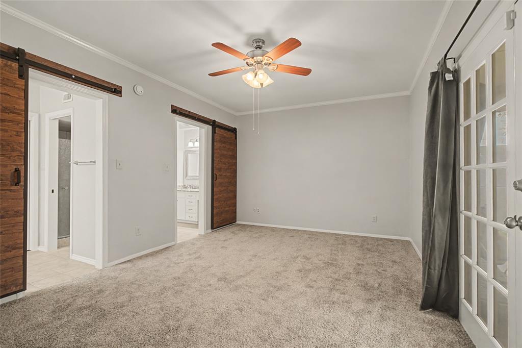 3200 Hickory Court Bedford, TX 76021 - Photo 16 of 30 Unfurnished bedroom featuring a barn door, light colored carpet, crown molding, ceiling fan, and ensuite bath