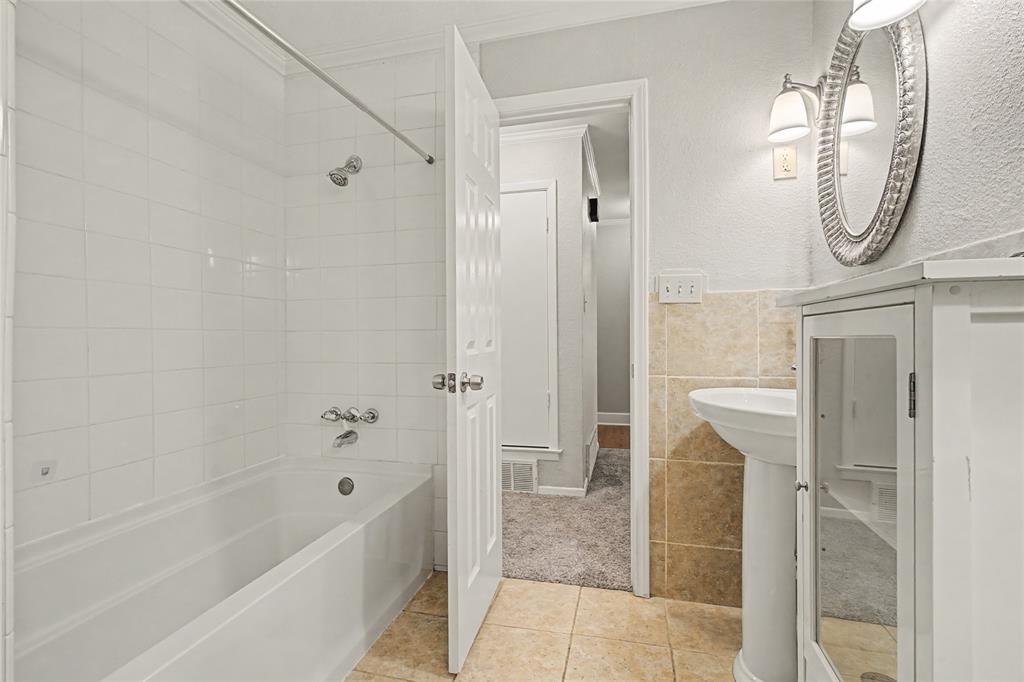 3200 Hickory Court Bedford, TX 76021 - Photo 22 of 30 Bathroom featuring shower combination, tile walls, a textured wall, light tile patterned floors, and a wainscoted wall