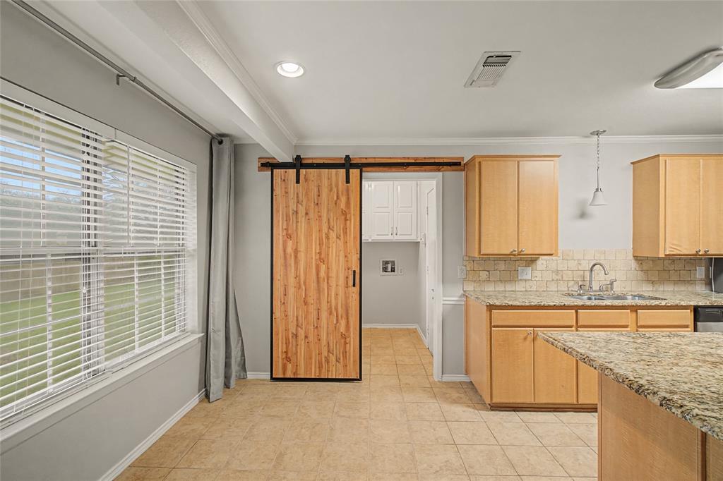 3200 Hickory Court Bedford, TX 76021 - Photo 24 of 30 Kitchen with a barn door, light wood finish cabinetry, light stone countertops, ornamental molding, and tasteful backsplash