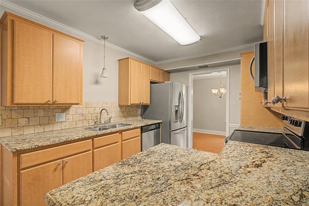 3200 Hickory Court Bedford, TX 76021 - Photo 9 of 30 Kitchen with light stone countertops, stainless steel appliances, backsplash, a chandelier, and ornamental molding