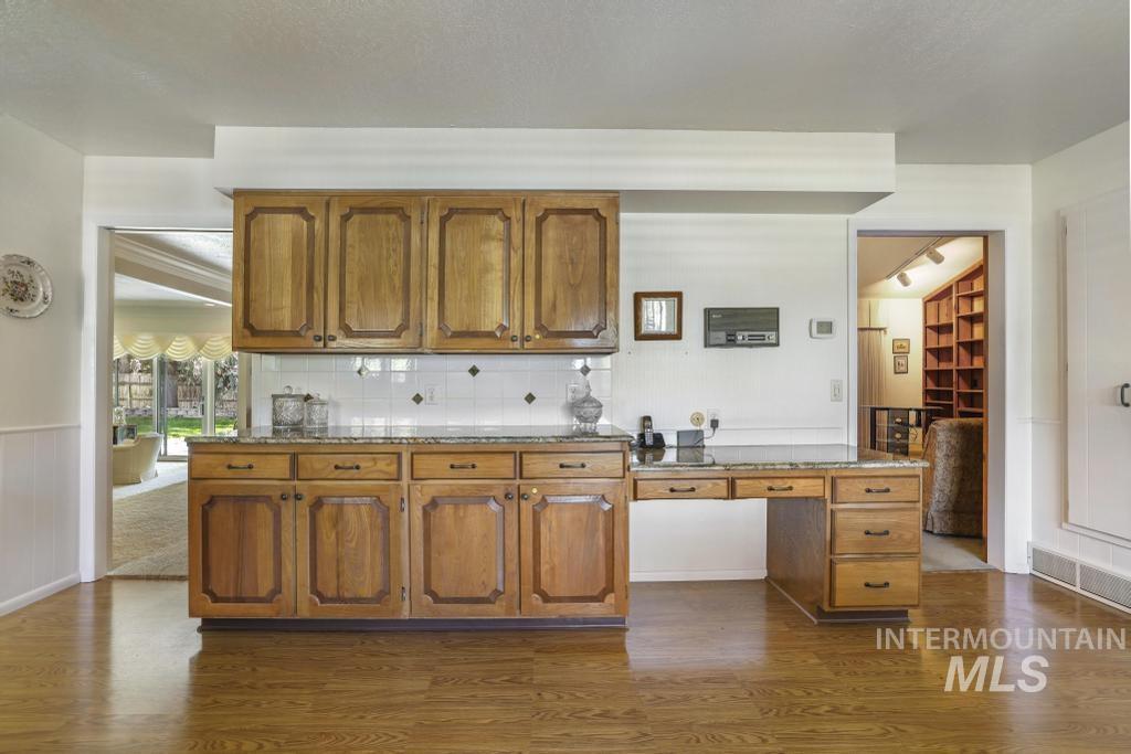2018 Rancho Vista Drive Twin Falls, ID 83301 - Photo 16 of 50 Kitchenette featuring wood-finish cabinetry, stone countertops, a white tile backsplash with decorative accents, and wood-finish flooring