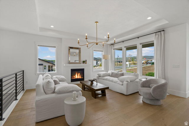 3349 Oxford Loop Morgan, UT 84050 - Photo 12 of 47 Living area featuring a chandelier, a raised ceiling, light wood-type flooring, plenty of natural light, and a glass covered fireplace