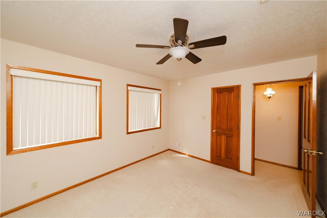 2100 East Valley View Road Kingman, AZ 86409 - Photo 30 of 53 Carpeted interior room featuring two windows with vertical blinds, a ceiling fan with integrated lighting, and wood-paneled doors with brass hardware