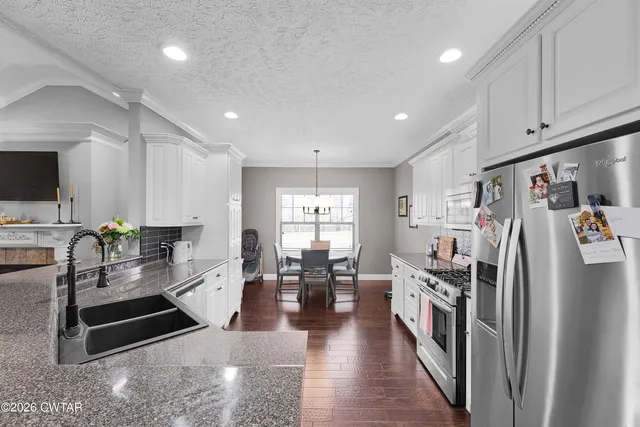 a kitchen with stainless steel appliances granite countertop a refrigerator a stove a sink dishwasher and white cabinets with wooden floor