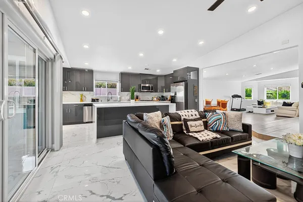 a living room with stainless steel appliances kitchen island granite countertop a refrigerator a sink dishwasher a dining table and chairs with wooden floor
