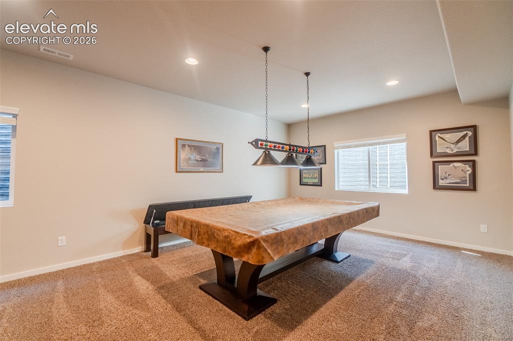 1061 Native Dancer Terrace Colorado Springs, CO 80921 - Photo 38 of 50 Recessed lighting illuminates the carpeted room, featuring a window with horizontal blinds and a pool table with a dedicated overhead light fixture