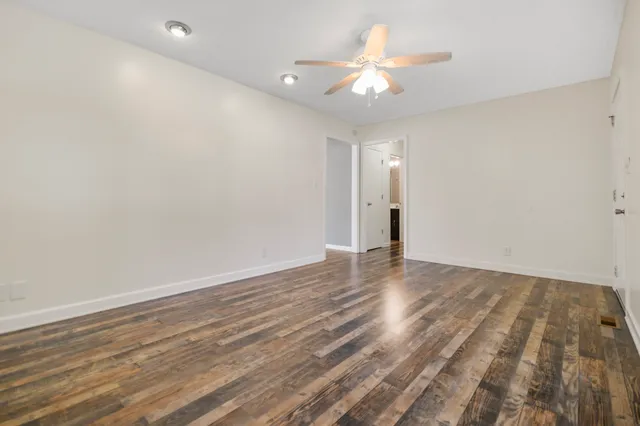 a view of an empty room with wooden floor and a ceiling fan