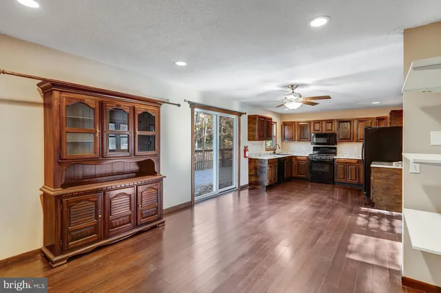 a living room with stainless steel appliances kitchen island granite countertop a refrigerator a stove a sink and a dining table with wooden floor