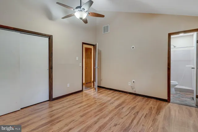 a view of an empty room with wooden floor and a ceiling fan