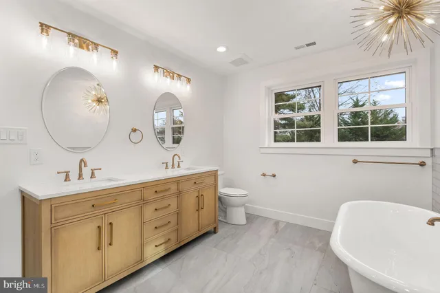 a spacious bathroom with a double vanity sink a large mirror and a toilet
