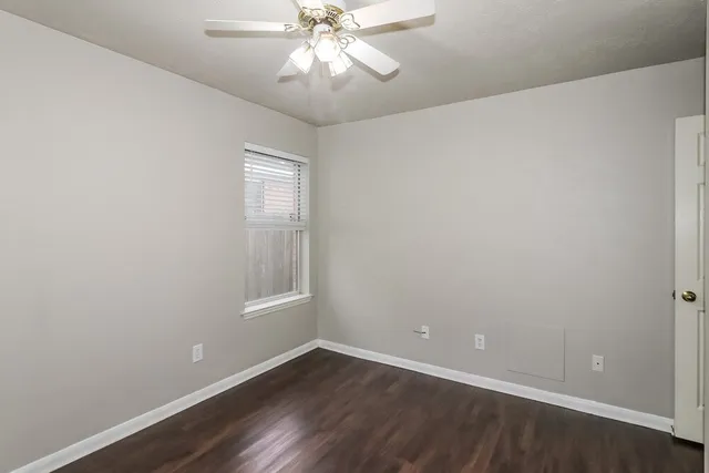 an empty room with wooden floor chandelier fan and windows