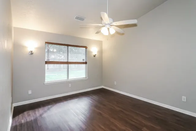 an empty room with wooden floor fan and windows