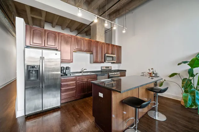 a kitchen with stainless steel appliances granite countertop a refrigerator a sink a stove and a wooden floors