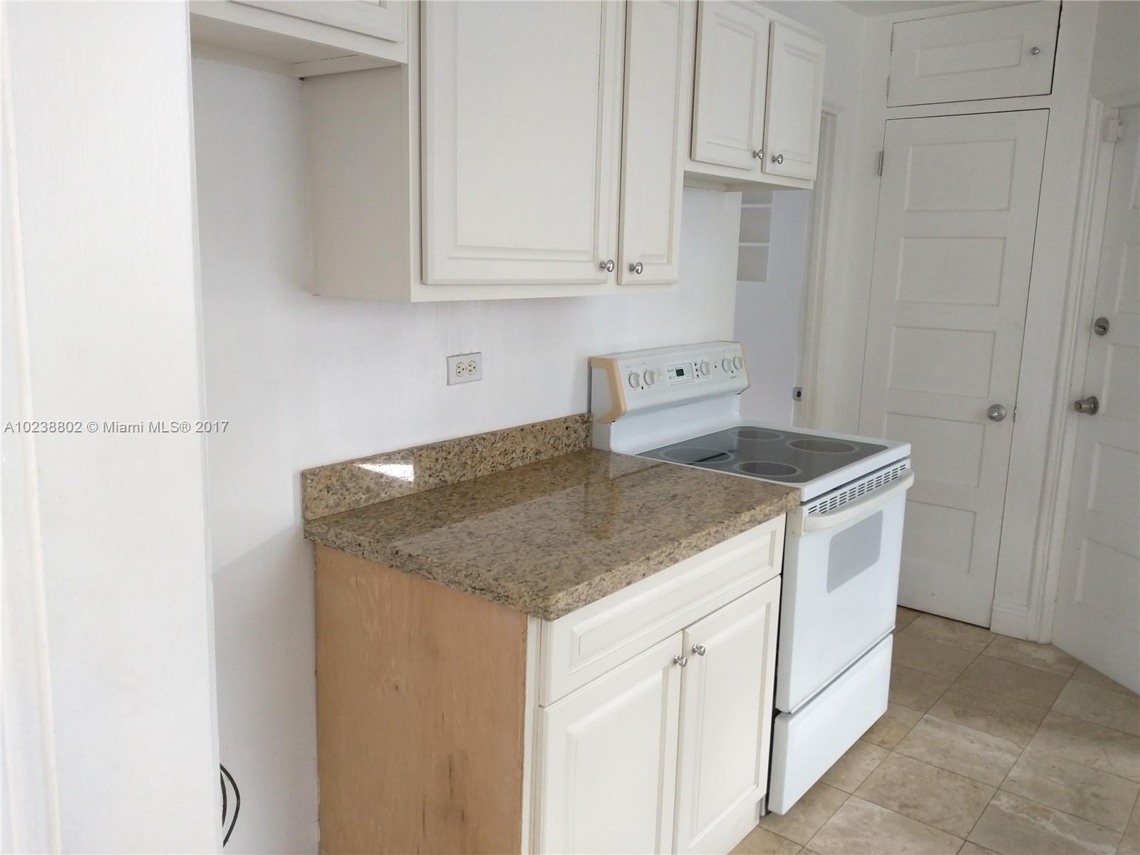 4717 Alton Road Miami Beach, FL 33140 - Photo 7 of 34 a kitchen with granite countertop white cabinets and white appliances