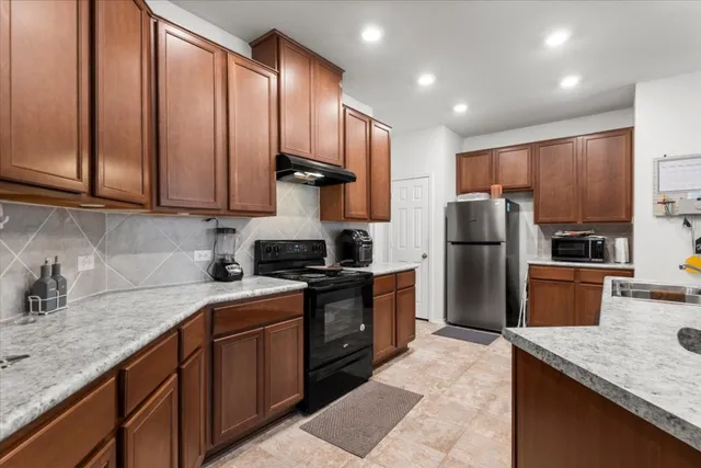 a kitchen with stainless steel appliances granite countertop a refrigerator a sink a stove a oven and white cabinets with wooden floors