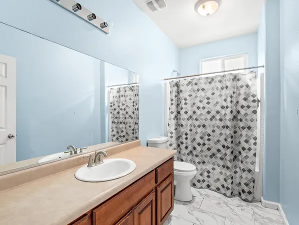 a bathroom with a granite countertop toilet a sink a mirror a window and a shower